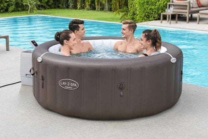 Lay Z Spa Dominica inflatable HydroJet jacuzzi with four people relaxing by the poolside in a garden setting