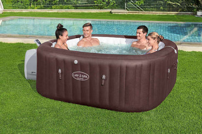 Lay Z Spa Maldives inflatable outdoor jacuzzi with four people enjoying HydroJet PRO massage on a green lawn by a pool