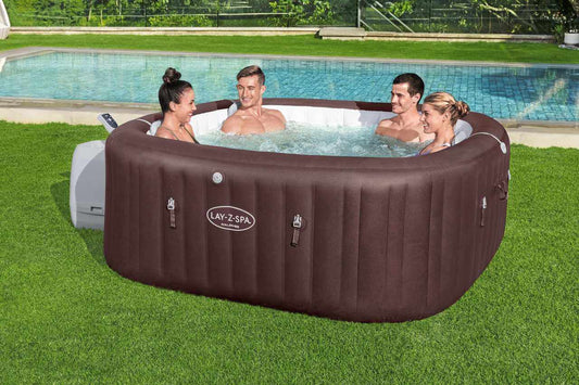Lay Z Spa Maldives inflatable outdoor jacuzzi with four people enjoying HydroJet PRO massage on a green lawn by a pool