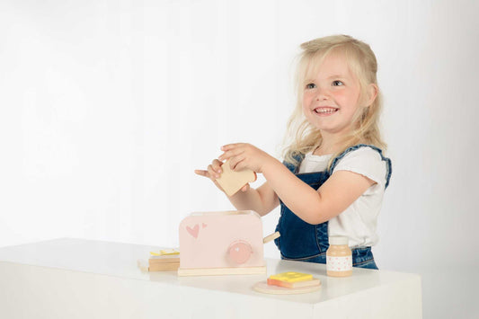 Child playing with pink wooden Label Label toster toy and accessories on white table