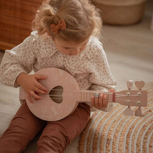 Dziecko grające na różowym drewnianym banjo Label Label z sercowym otworem rezonansowym.