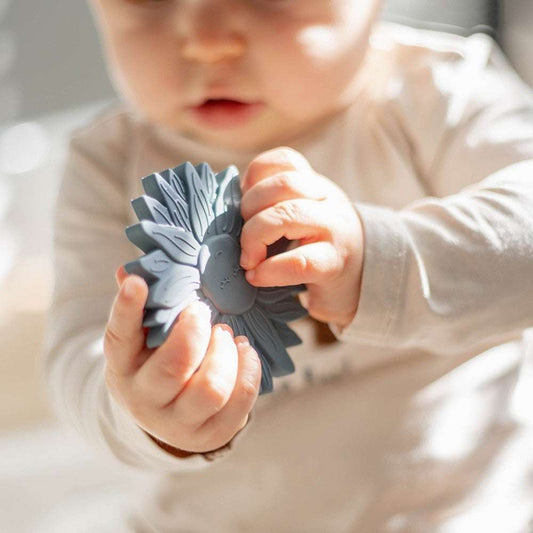 Dziecko trzyma Label Label silikonowy gryzak w kształcie słonecznika, bezpieczny ekologiczny teether z drewna FSC i nietoksycznego silikonu.
